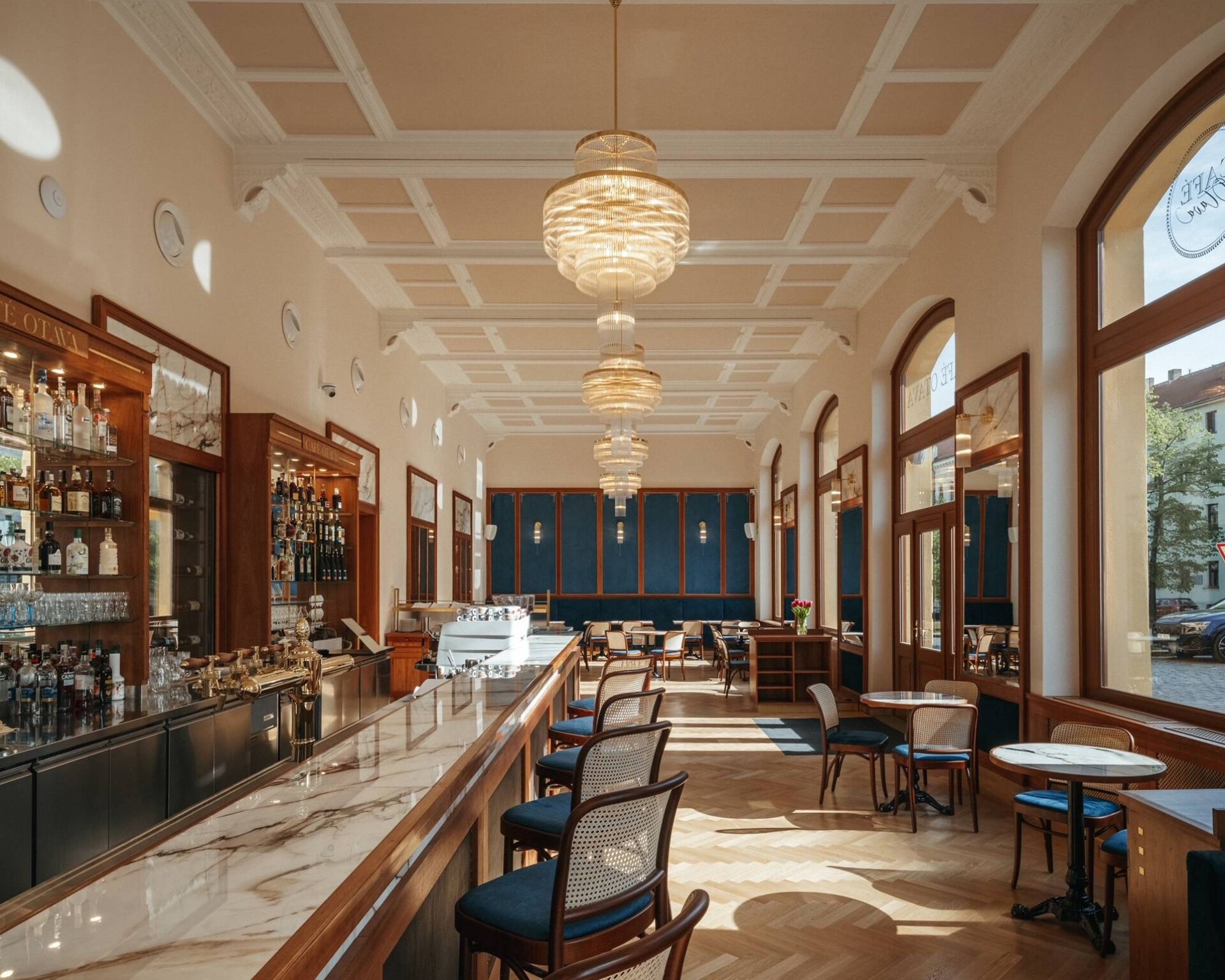 Барная зона у входа в Café Otava с мраморной столешницей, деревянной стойкой и тремя латунными люстрами под кессонным потолком